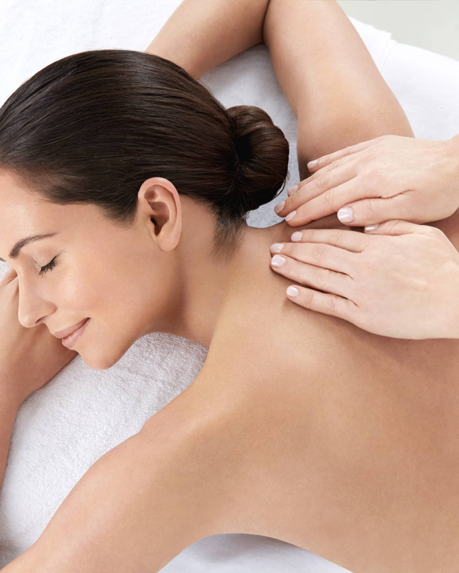 Woman smiles, lies on massage table as hands massage bare shoulders