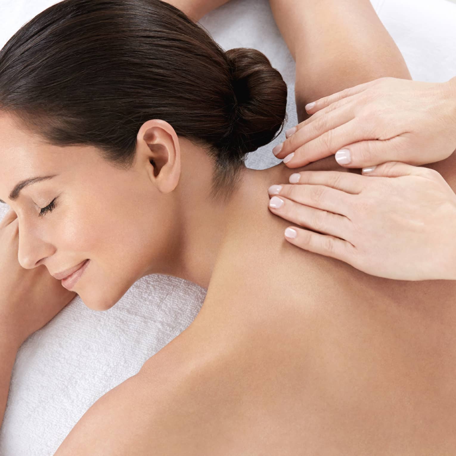 Woman smiles, lies on massage table as hands massage bare shoulders