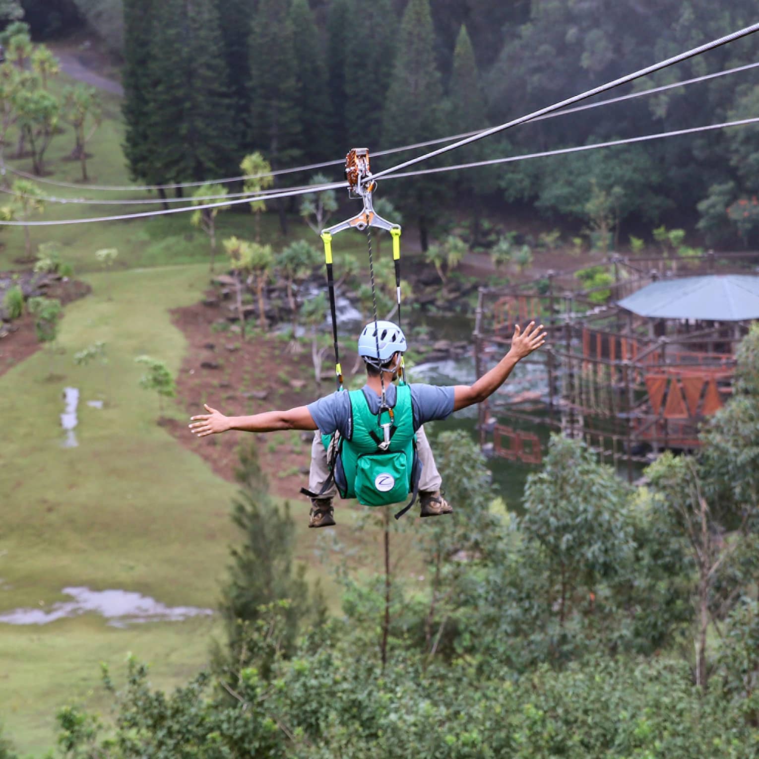 Adventure Park, two people glide down zip lines high above trees over mountain