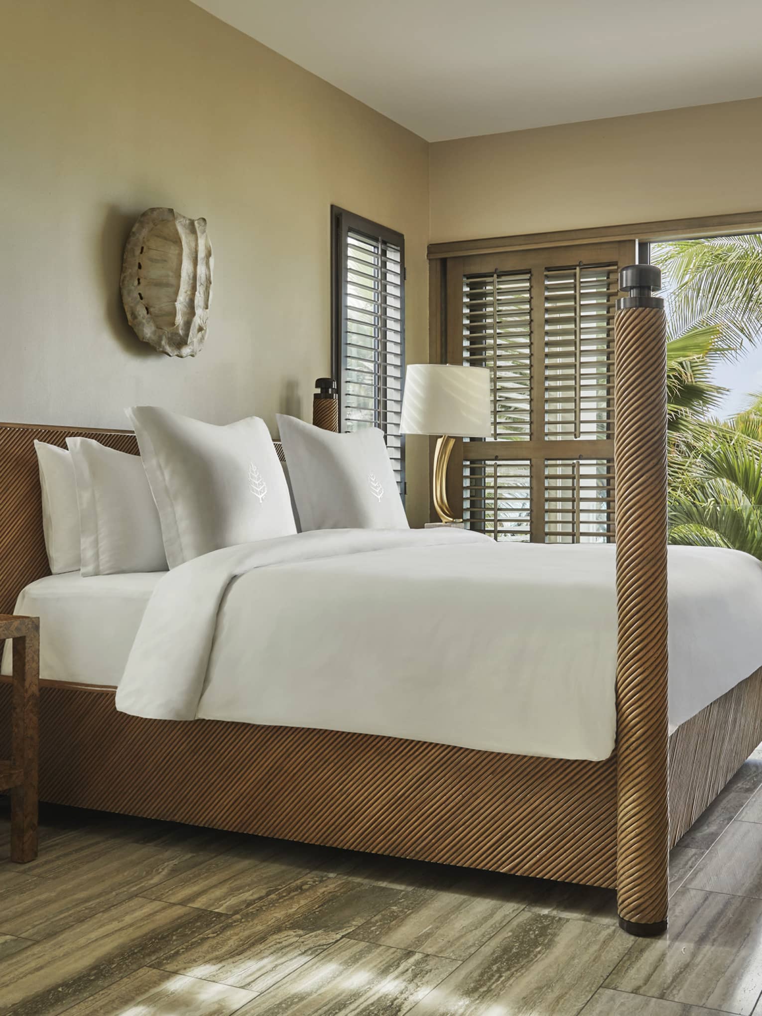 Bright bedroom with four-poster bed, wood accents and balcony view of palm trees and ocean