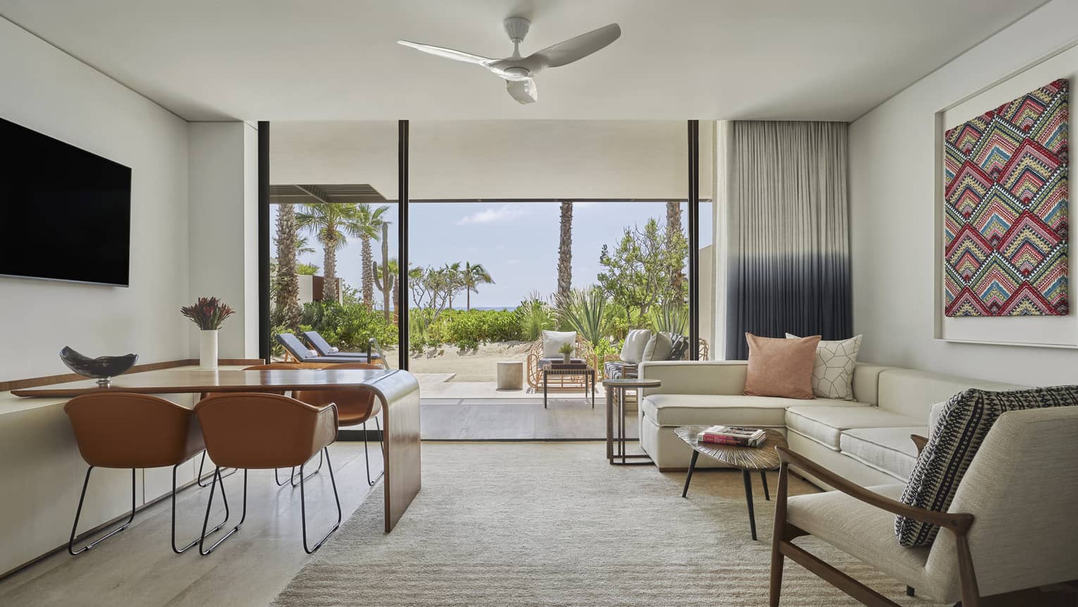 A hotel room with table, large sofa, large sliding glass doors and tv.