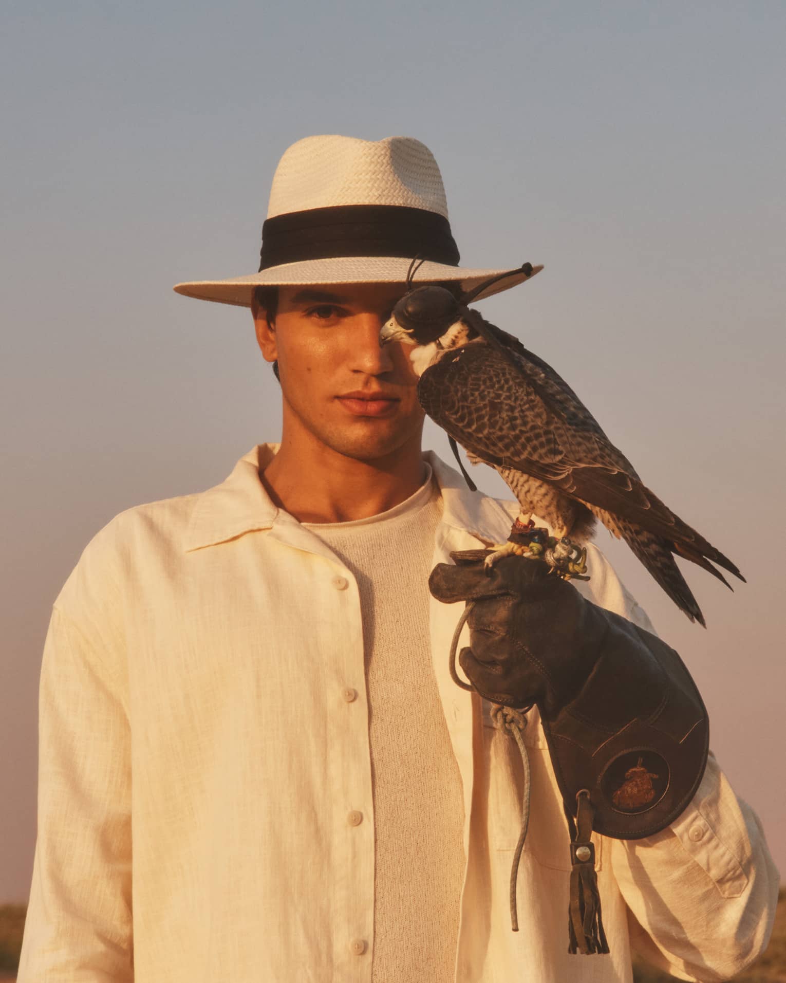 Person in straw hat and white shirt with gloved hand outstretched and hawk perched on it