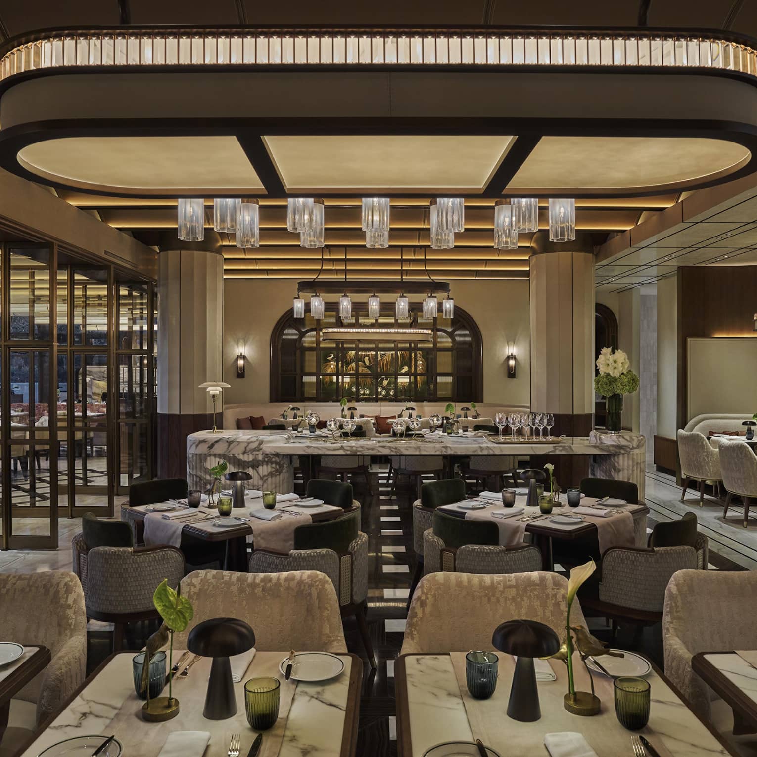 Restaurant dining room with grey and cream colour palatte, green florals on every table and a large overhead curved light piece