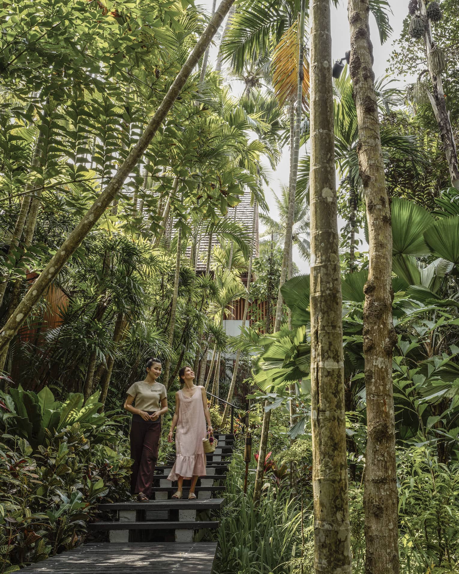 Female guest and spa staff member walk along foliage-lined pathway to the spa