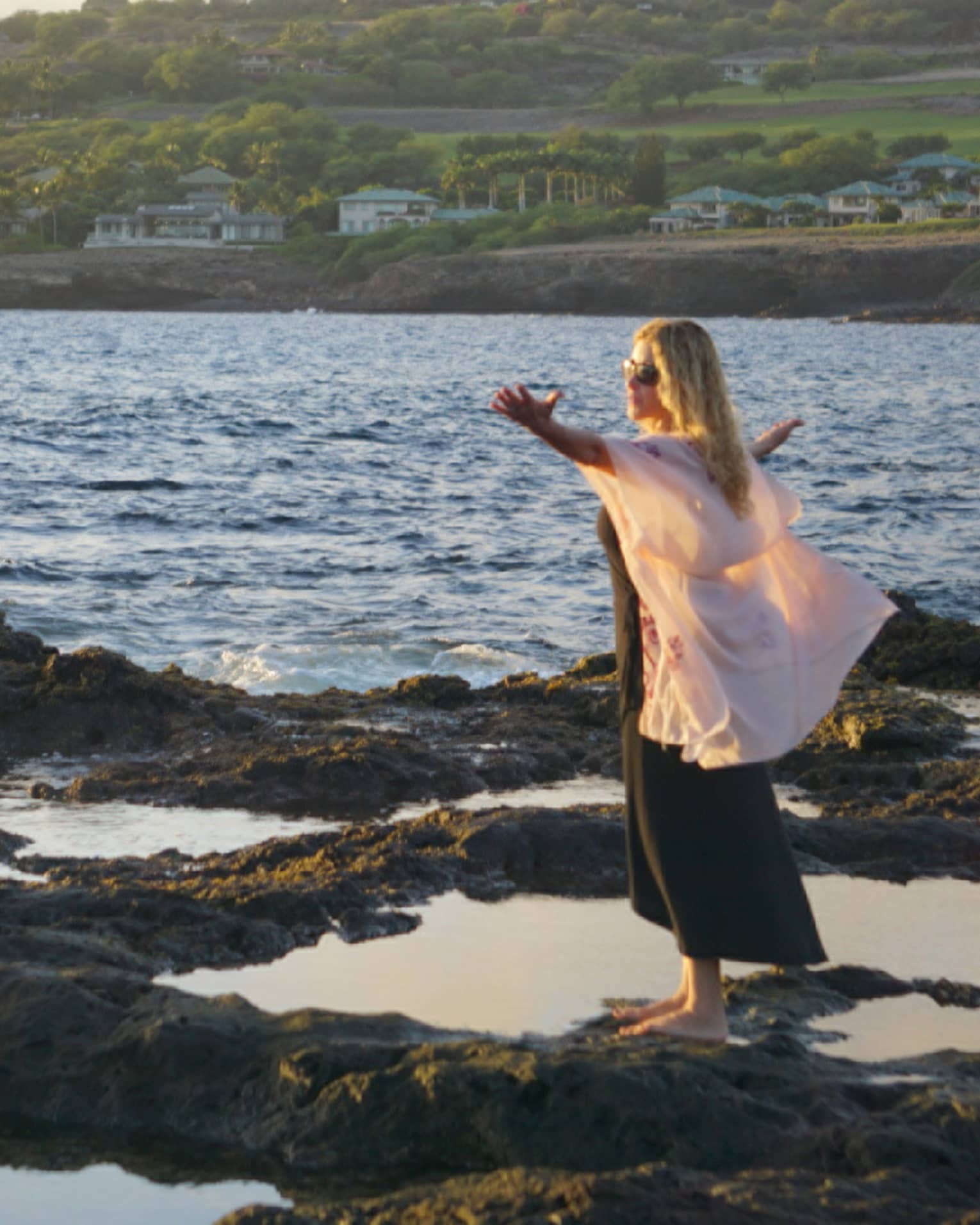 A woman meditates at edge of ocean on lava rock