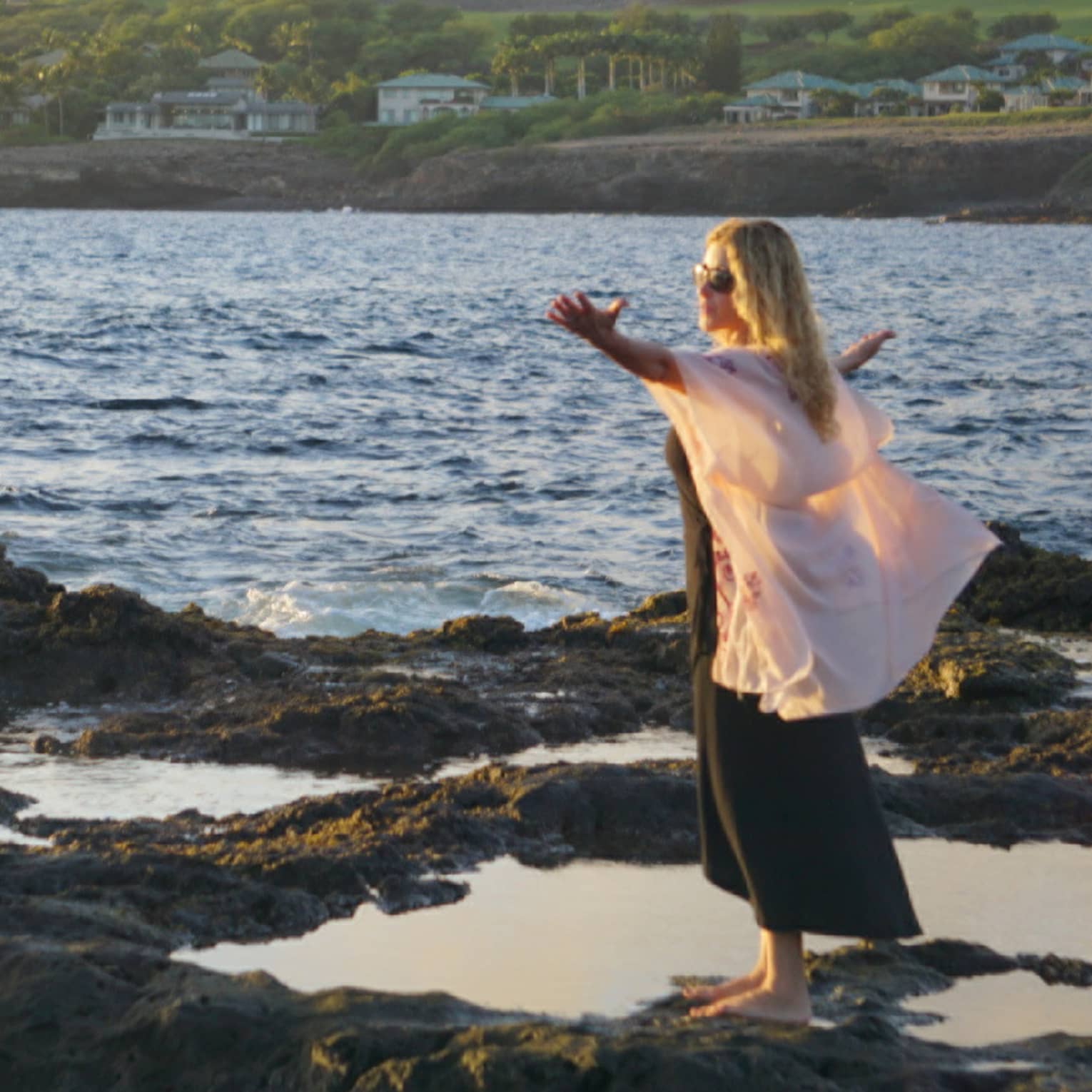 A woman meditates at edge of ocean on lava rock