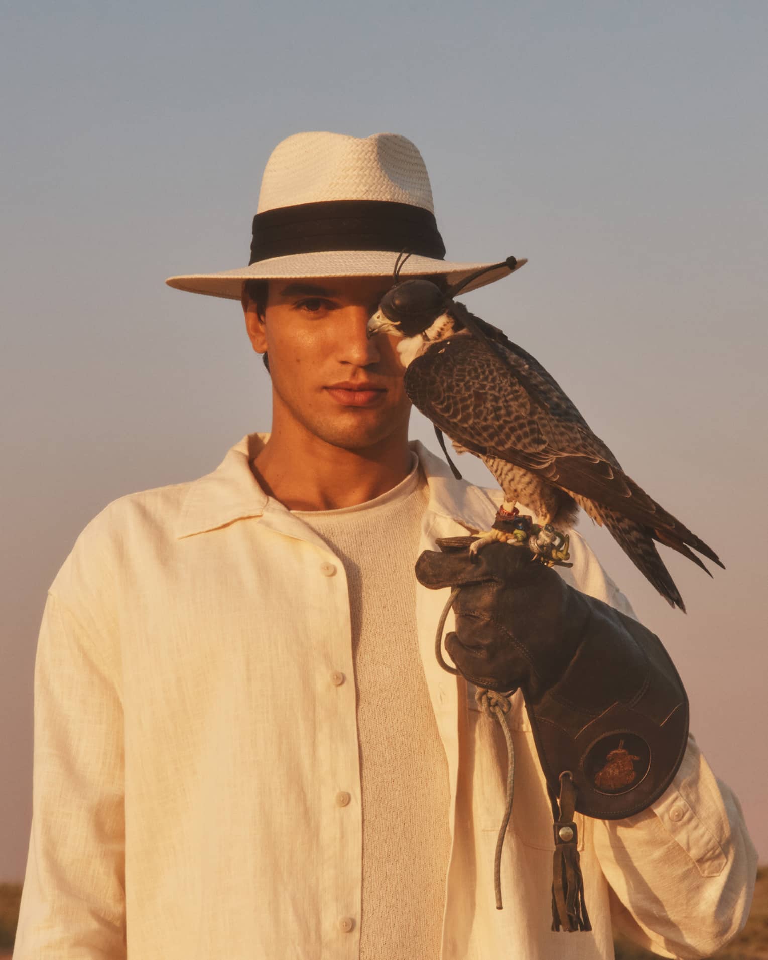 Person in straw hat and white shirt with gloved hand outstretched and hawk perched on it