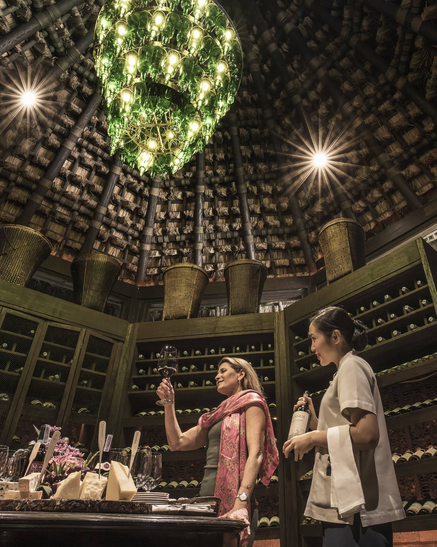 Two people in rustic wine cellar with a green bottle chandelier