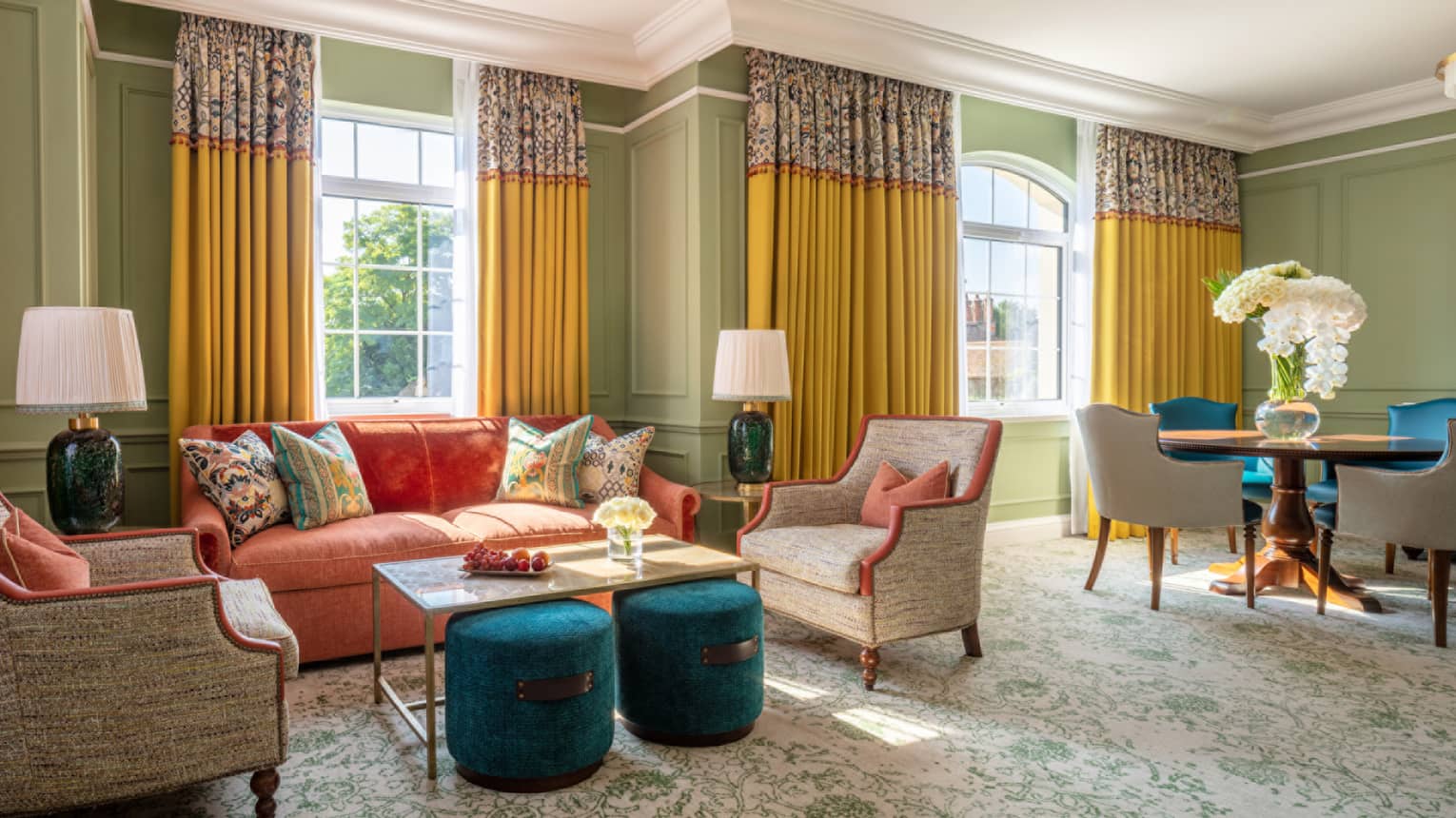 Guest room with red couch, two cream accent chairs and coffee table, dining table with four chairs, twin windows with yellow drapes