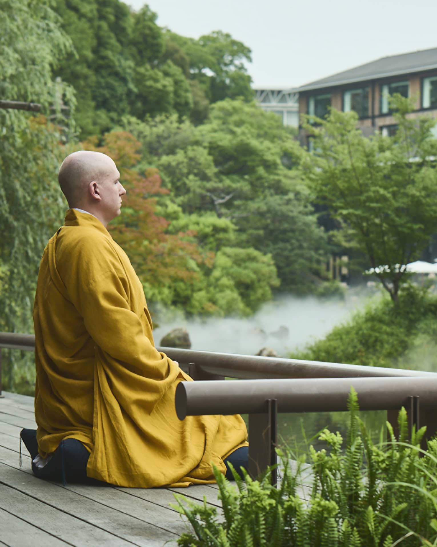A monk sits at the edge of a serene pond