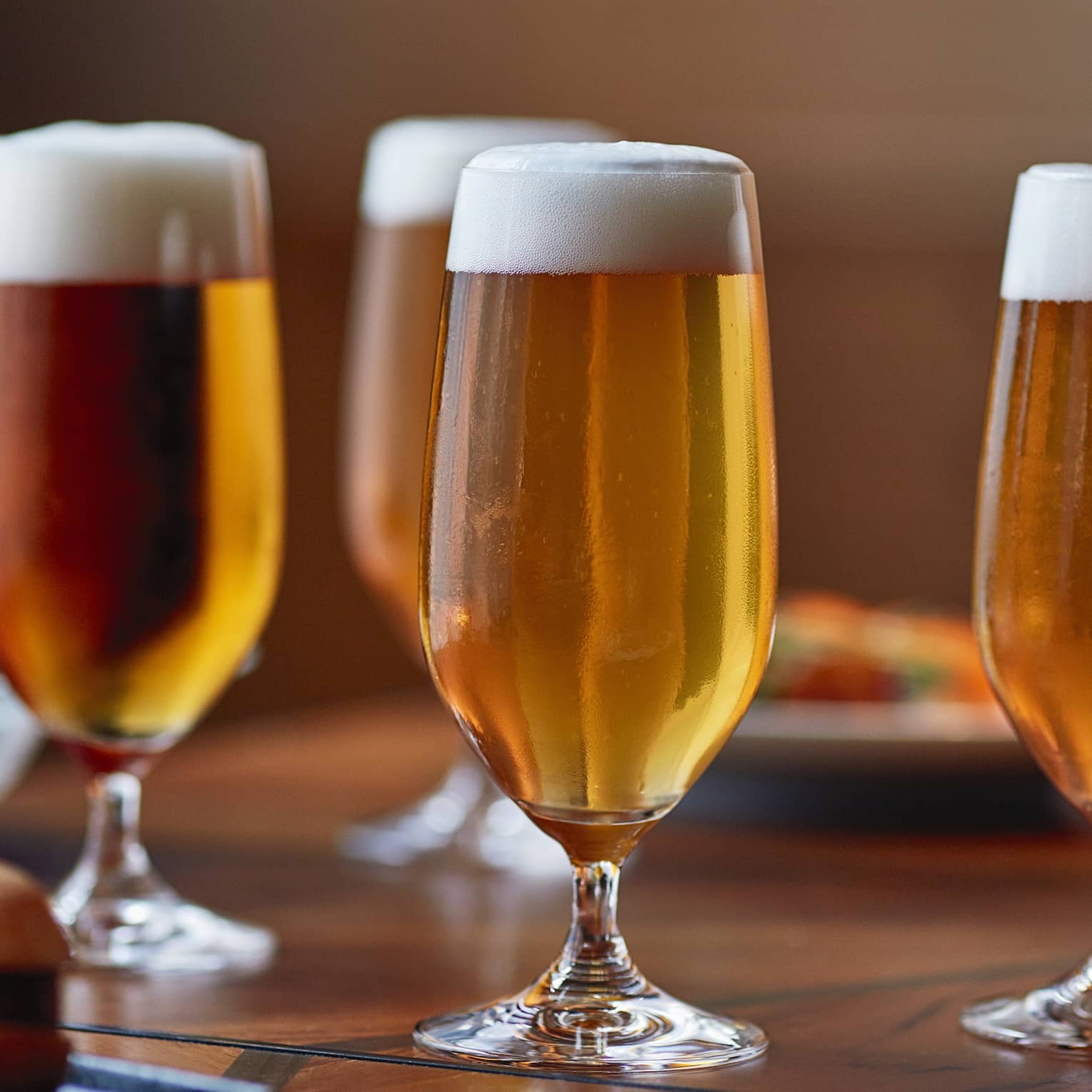 Four tall beer glasses filled with beer on a table with cheese, crackers and appetizers