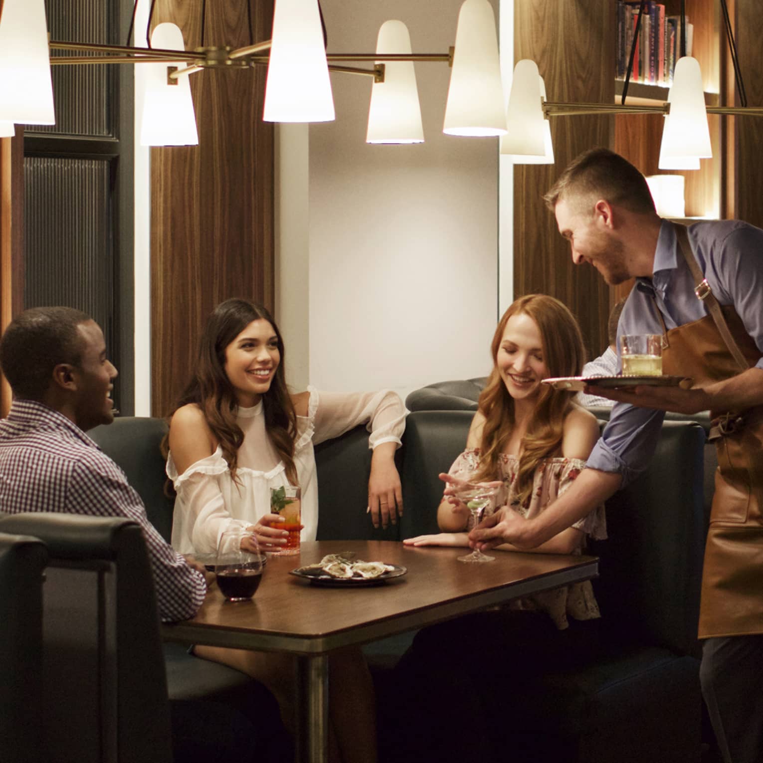 A man and two women being served drinks by a team member in a blue shirt and brown apron.