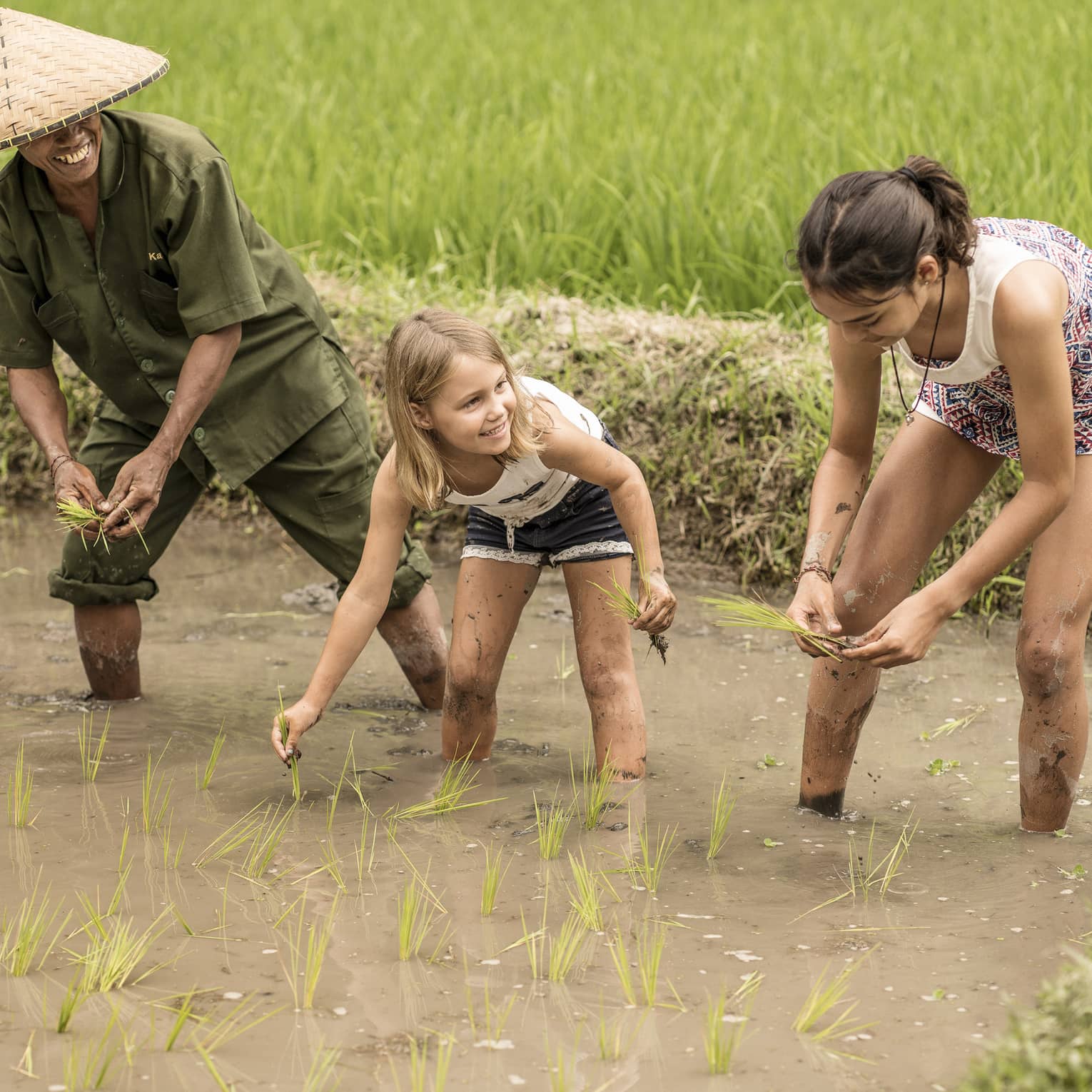 Four Seasons guests work in a rice field alongside a balinese farmer