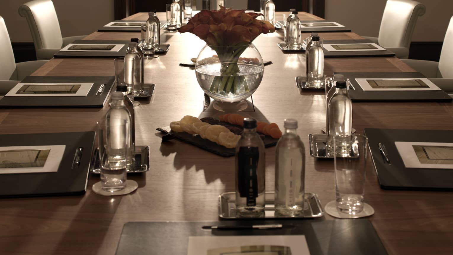Sleek leather chairs around large, dark wood boardroom table set for business event 