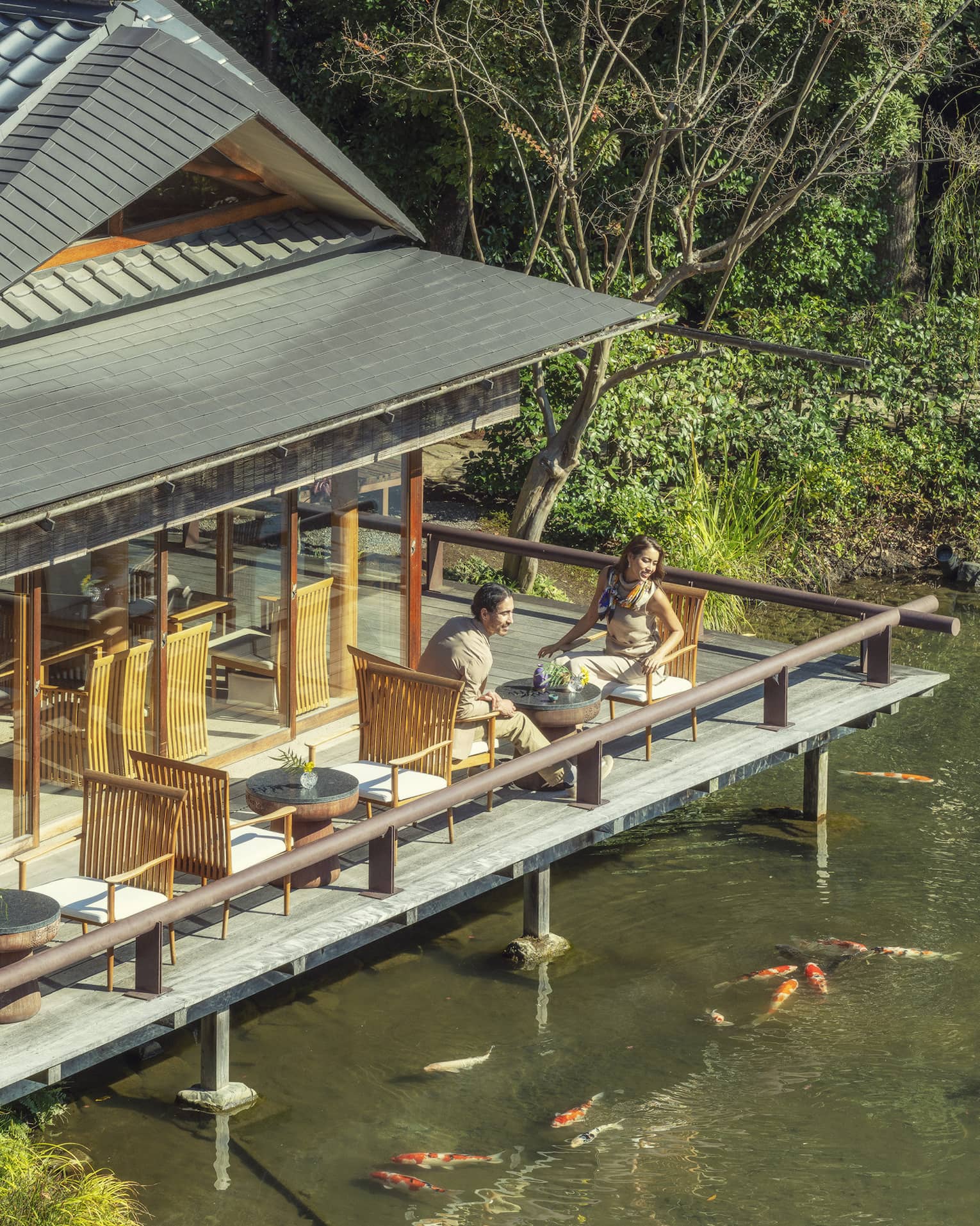 Two people sitting on an outdoor deck overlooking a pond with koi fish at Four Seasons