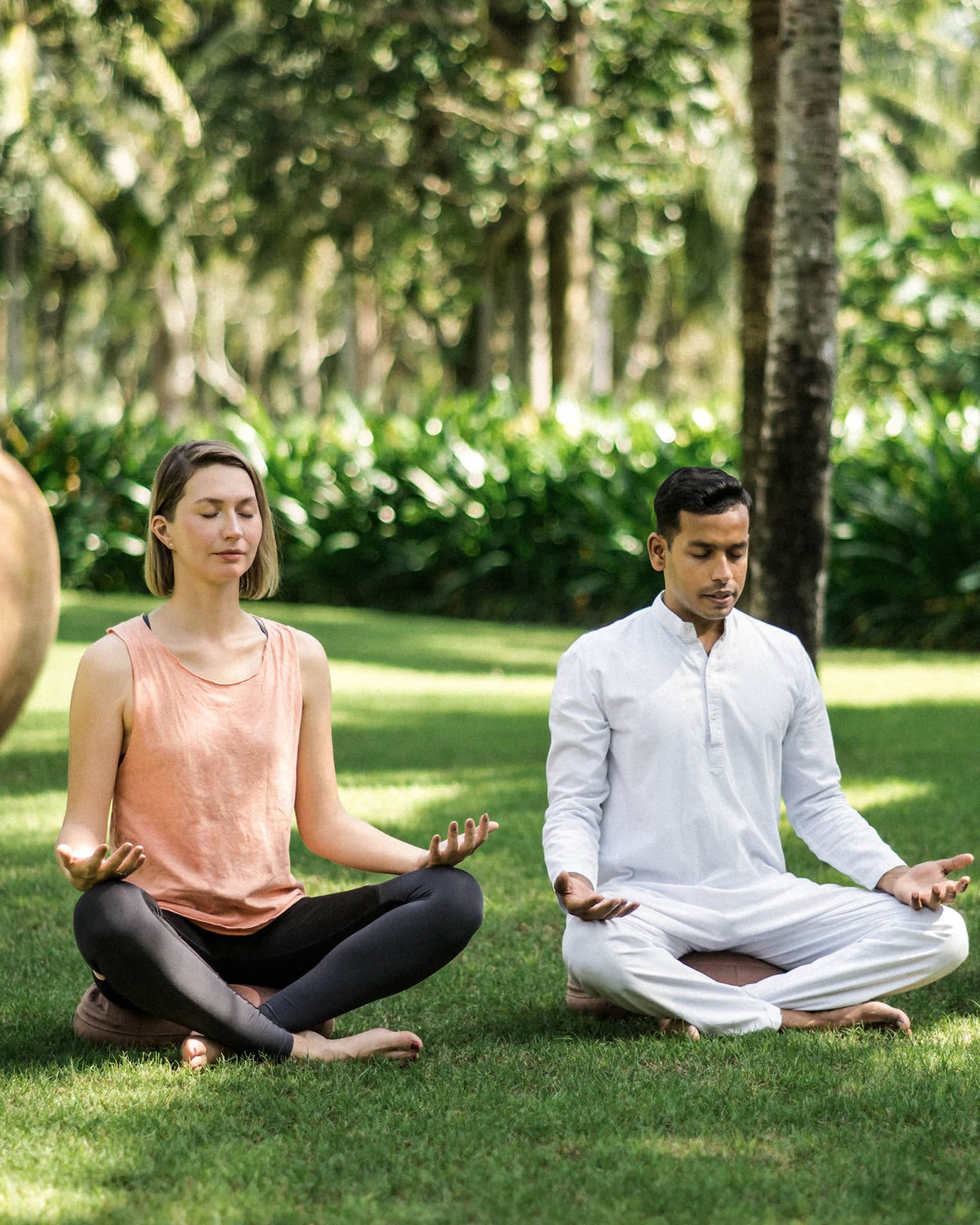 Two men and a woman practise meditation yoga outdoors on lawn
