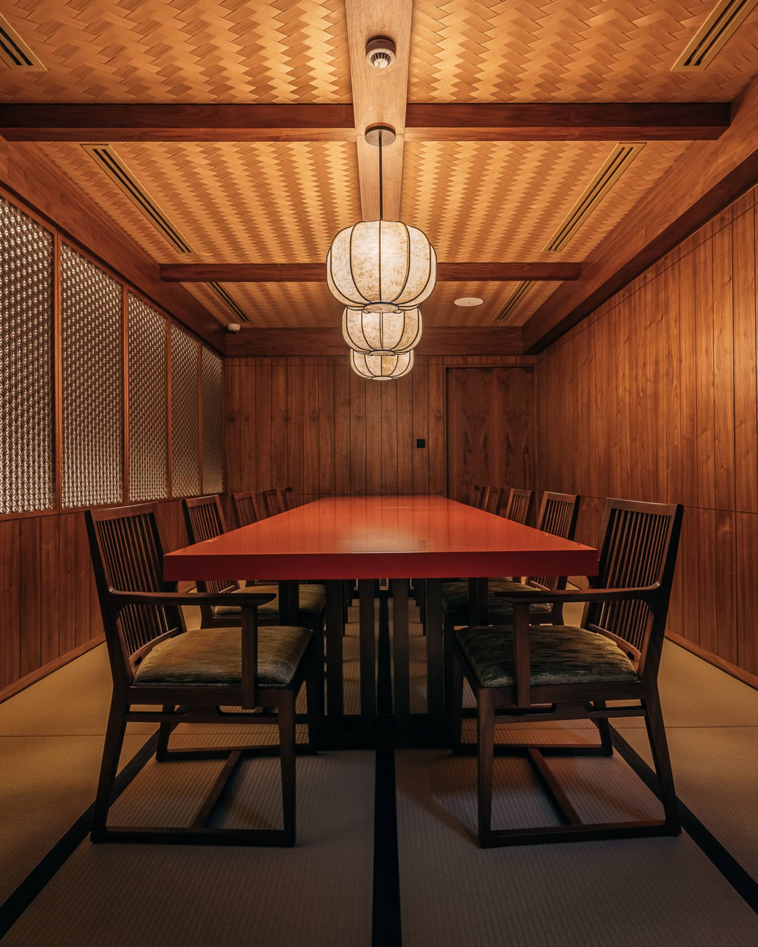 Private dining room with Japanese-style wood panelled walls and a red rectangular table in the centre sert beneath three paper lanterns