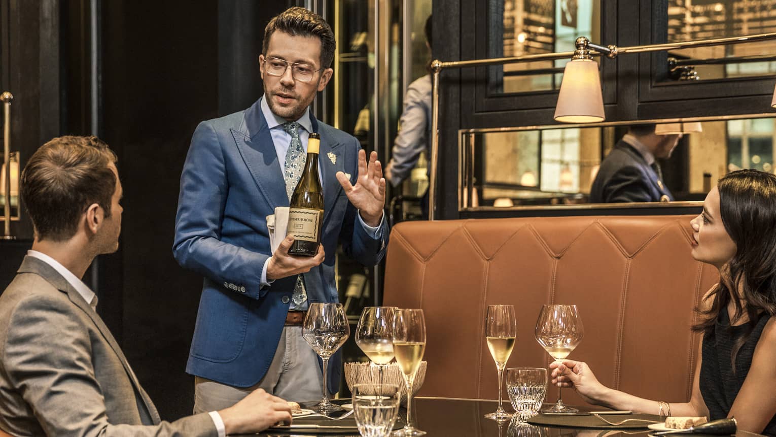 Couple with wine glasses in La Dame de Pic London booth while sommelier introduces bottle of white wine