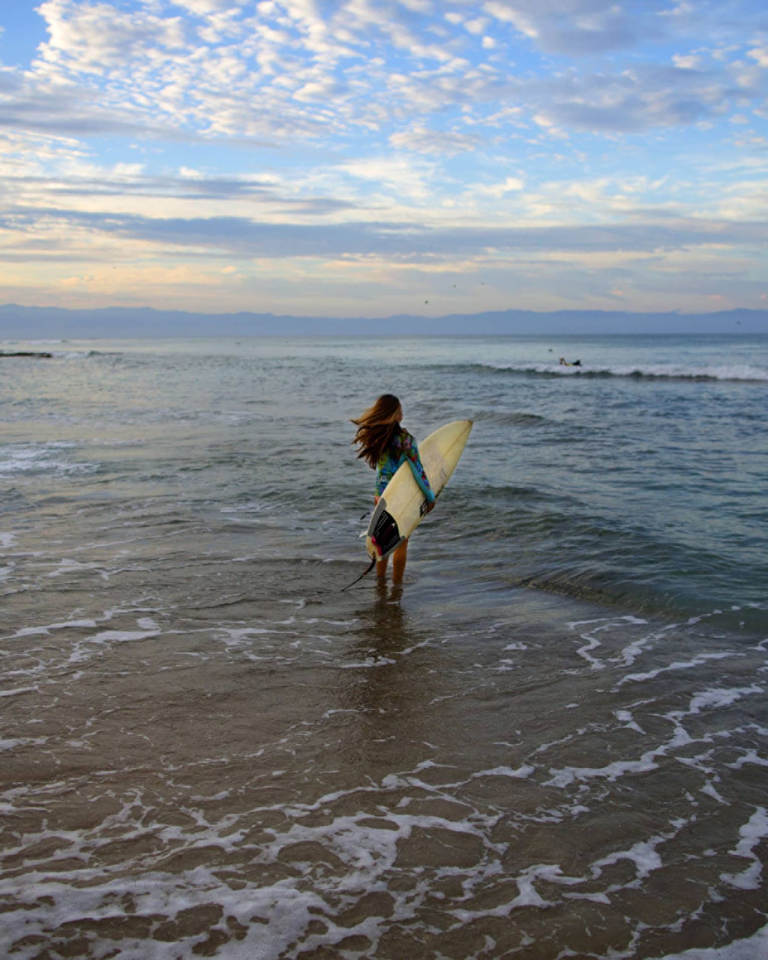 A woman holding a surfboard while walking towards ocean waves.