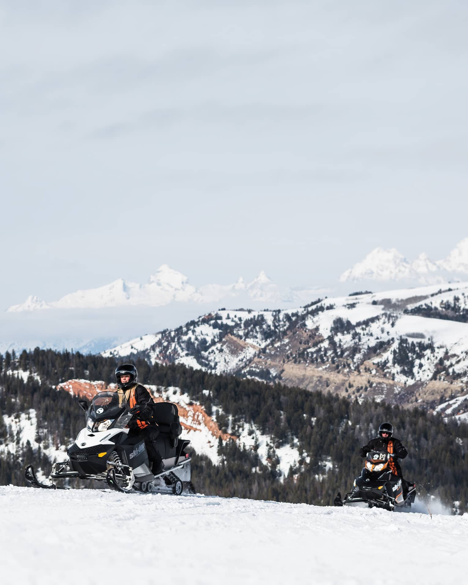 Person in snow gear on snowmobile with snowy mountain in backdrop