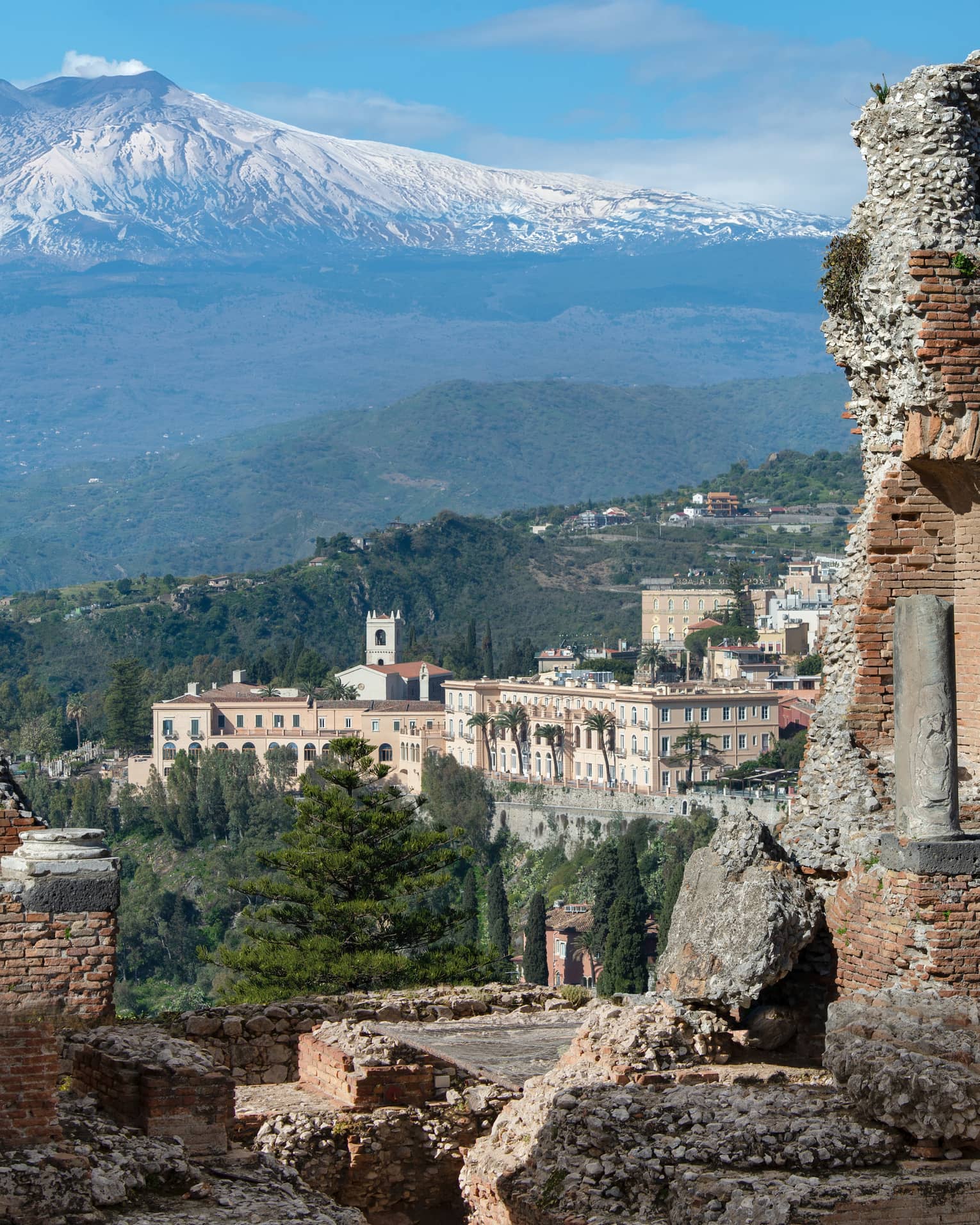 View of ancient stone ruins with a distant town and snow-capped mountains in the background.
