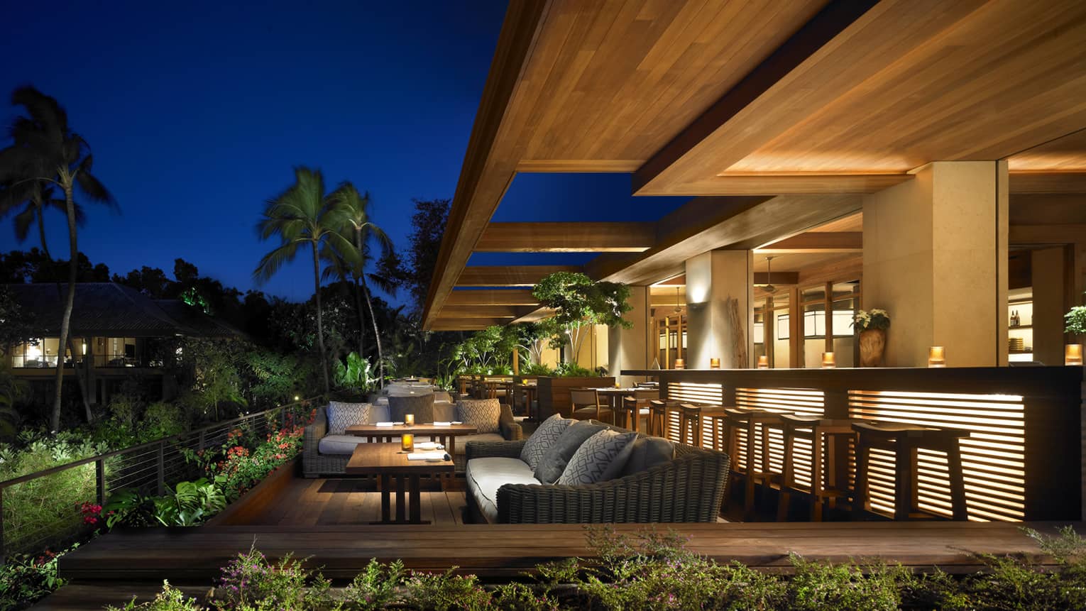 Patio sofas and lights by outdoor bar on wood deck under modern wood roof at night