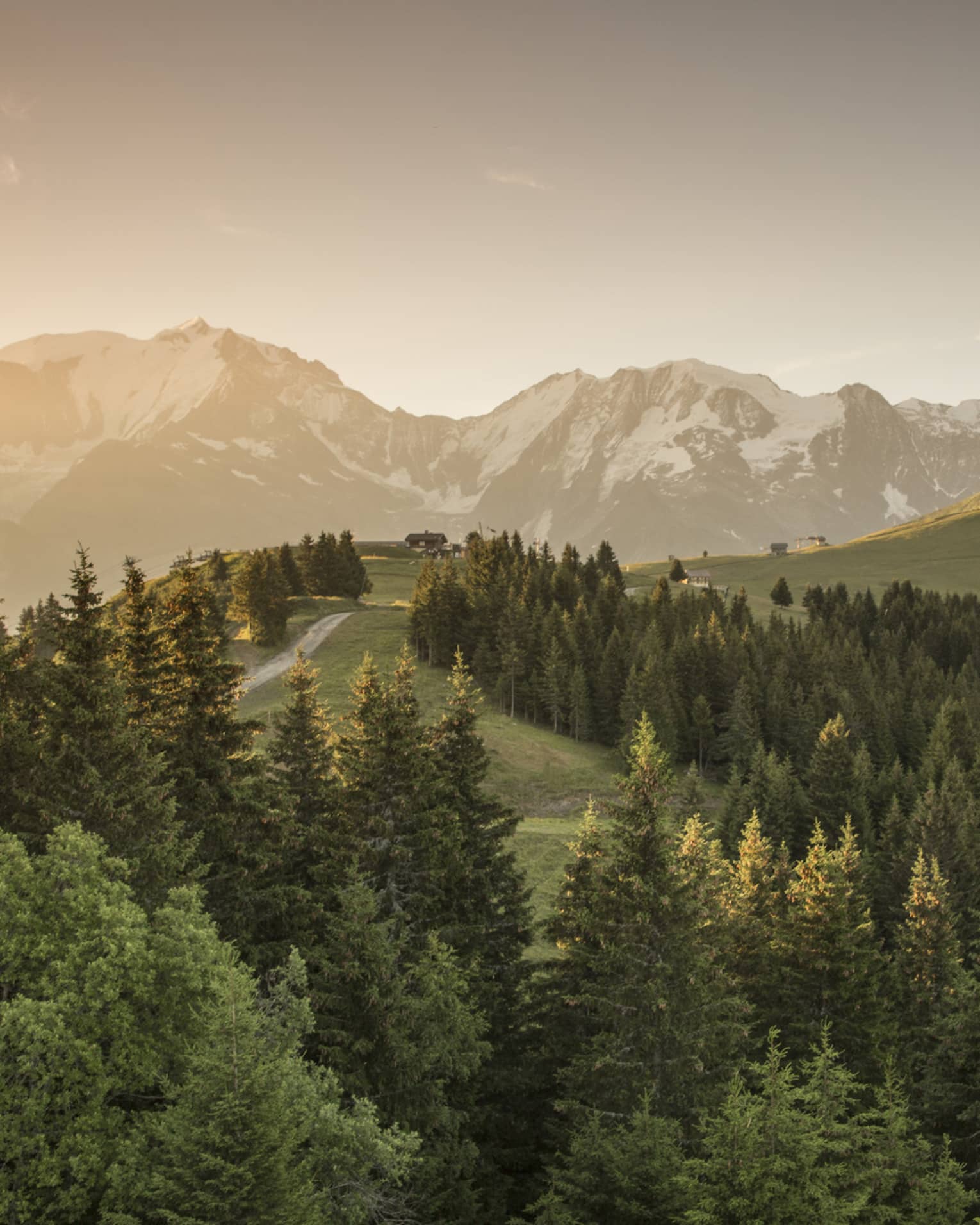 Sun sets over snow-capped mountains, green forests, trails in French Alps