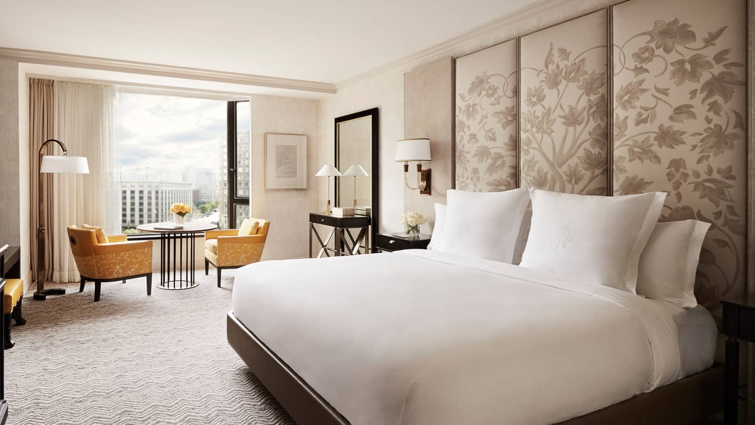 Deluxe City-View Room white bed with tall floral fabric headboard, black dresser, yellow velvet dining chairs by window
