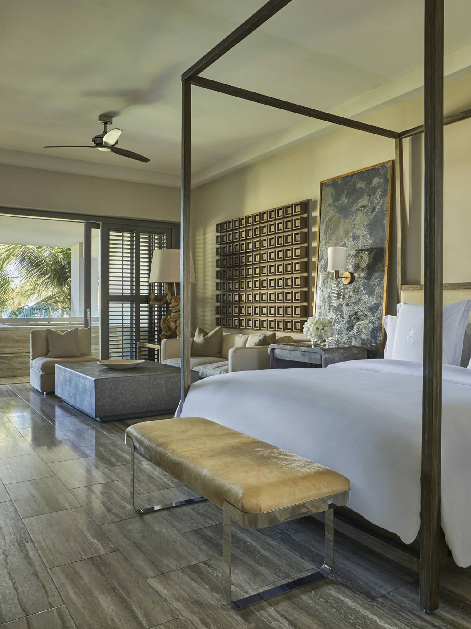 Spacious bedroom with a canopy bed, soft neutral décor, a bench at the foot and large windows overlooking a tropical garden