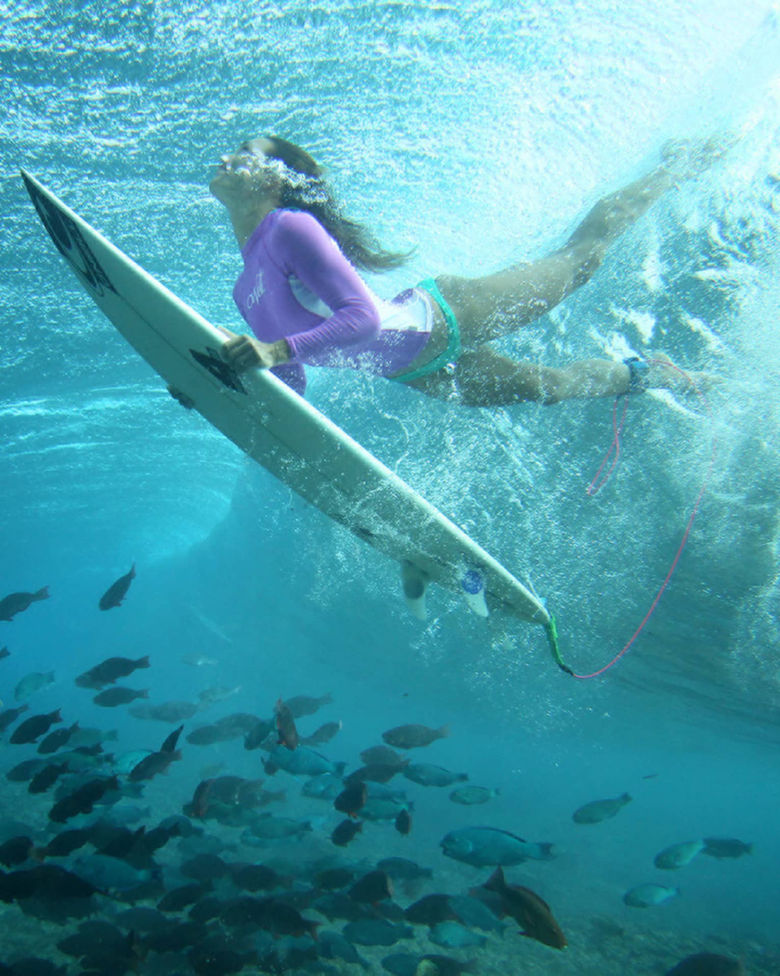 Céline Gehret, ascending from the water above a school of fish as she surfs in the Maldives