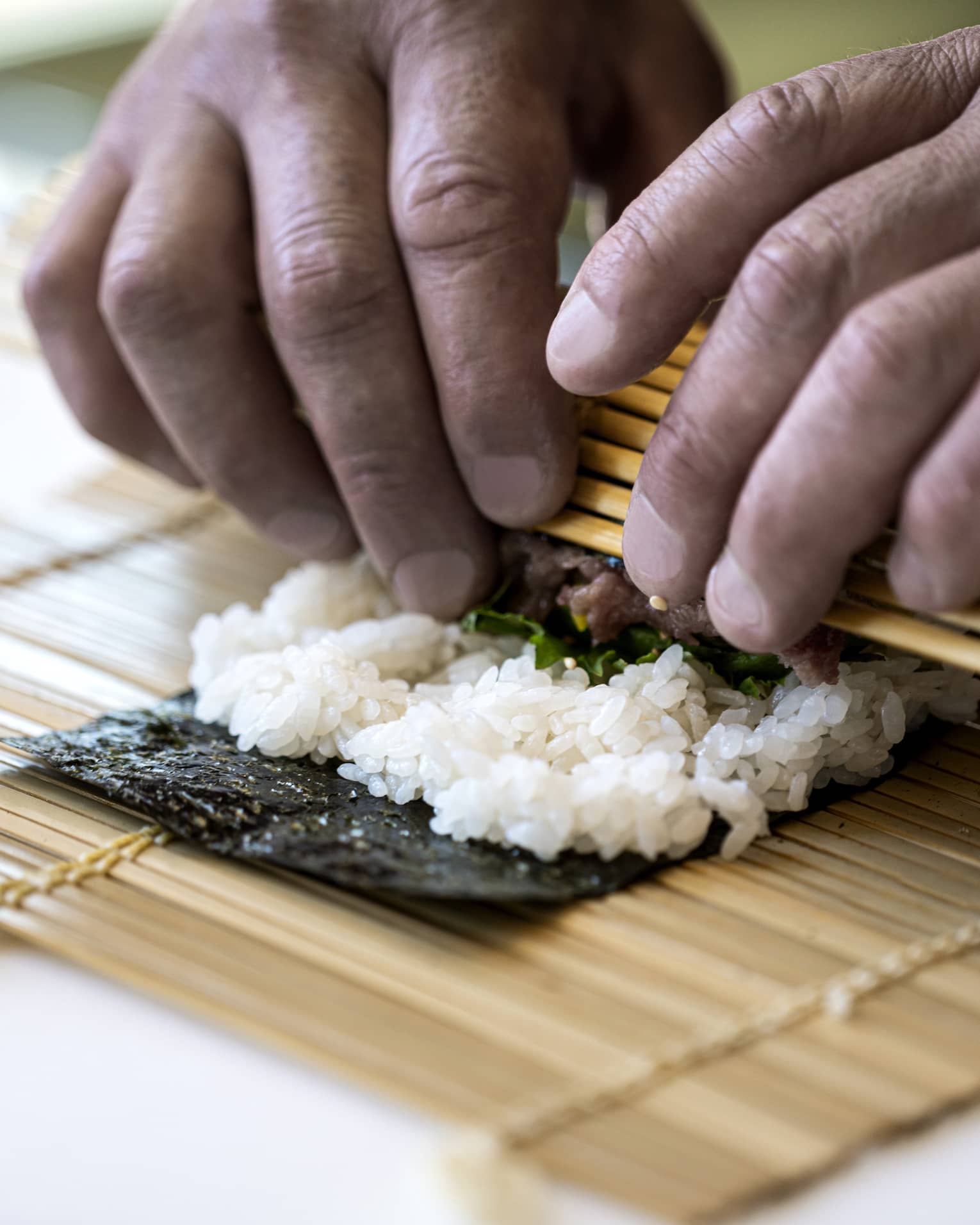A four seasons chef rolls sushi with a bamboo mat