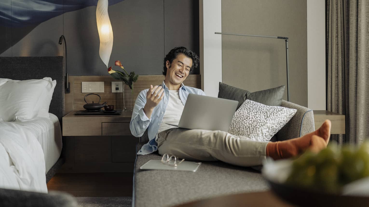Laughing man lounges on sofa with laptop in his guest room