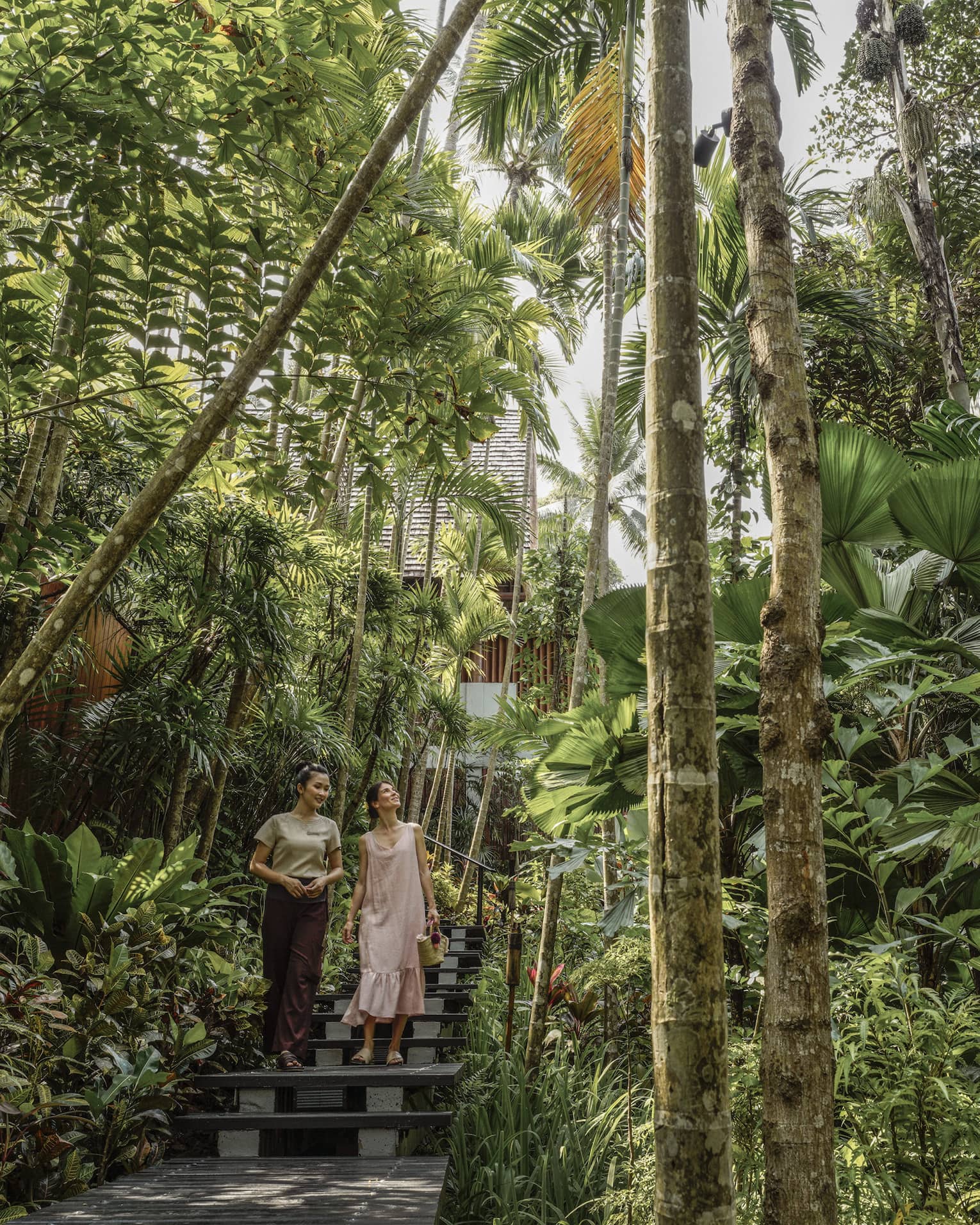 Female guest and spa staff member walk along foliage-lined pathway to the spa