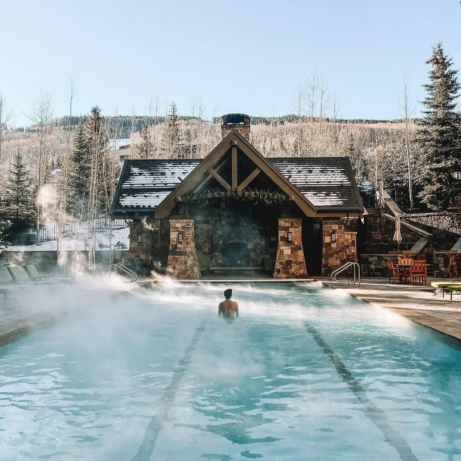 ,A man stands in the middle of a steaming heated outdoor swimming pool with a mountain view