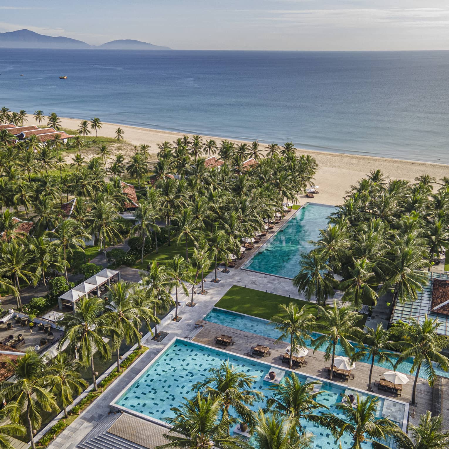 Aerial view of the resort pools with ocean views, palm trees and blue skies