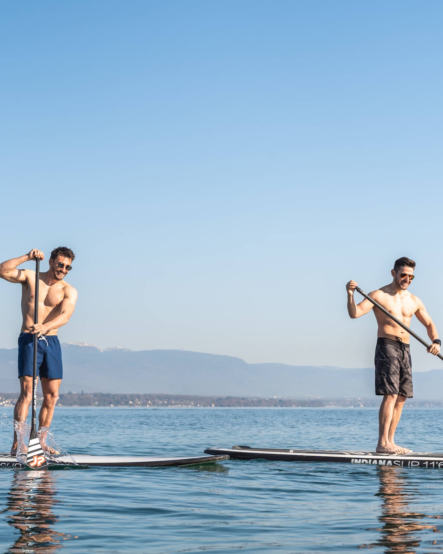 Two men stand-up paddleboarding on Lake Geneva