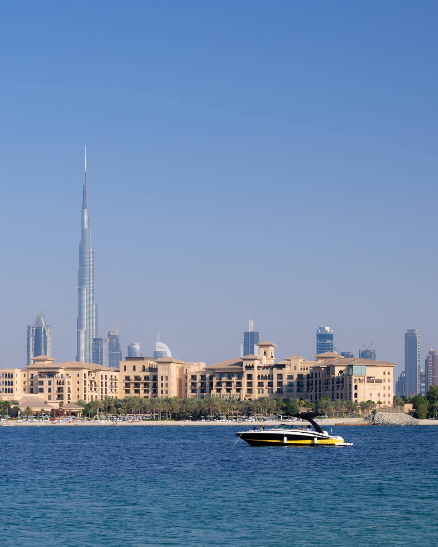 A white, yellow and black speed boat glides through the water with the Dubai skyline in the background