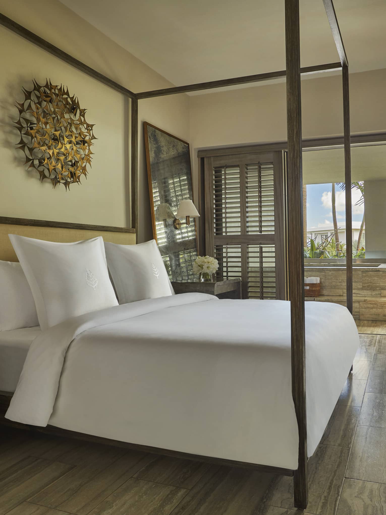 Elegant bedroom with canopy bed, wooden floors and a terrace view of palm trees and blue sky