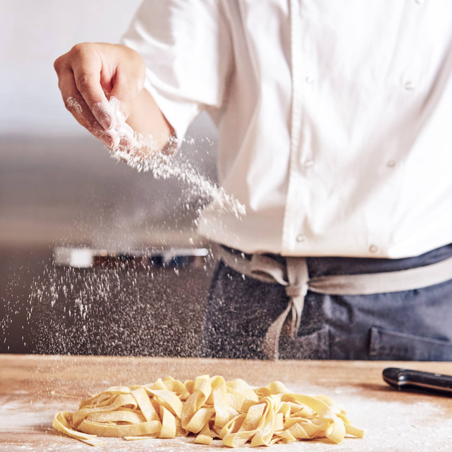 Noe chef sprinkles white flour over thick fresh pasta noodles on counter
