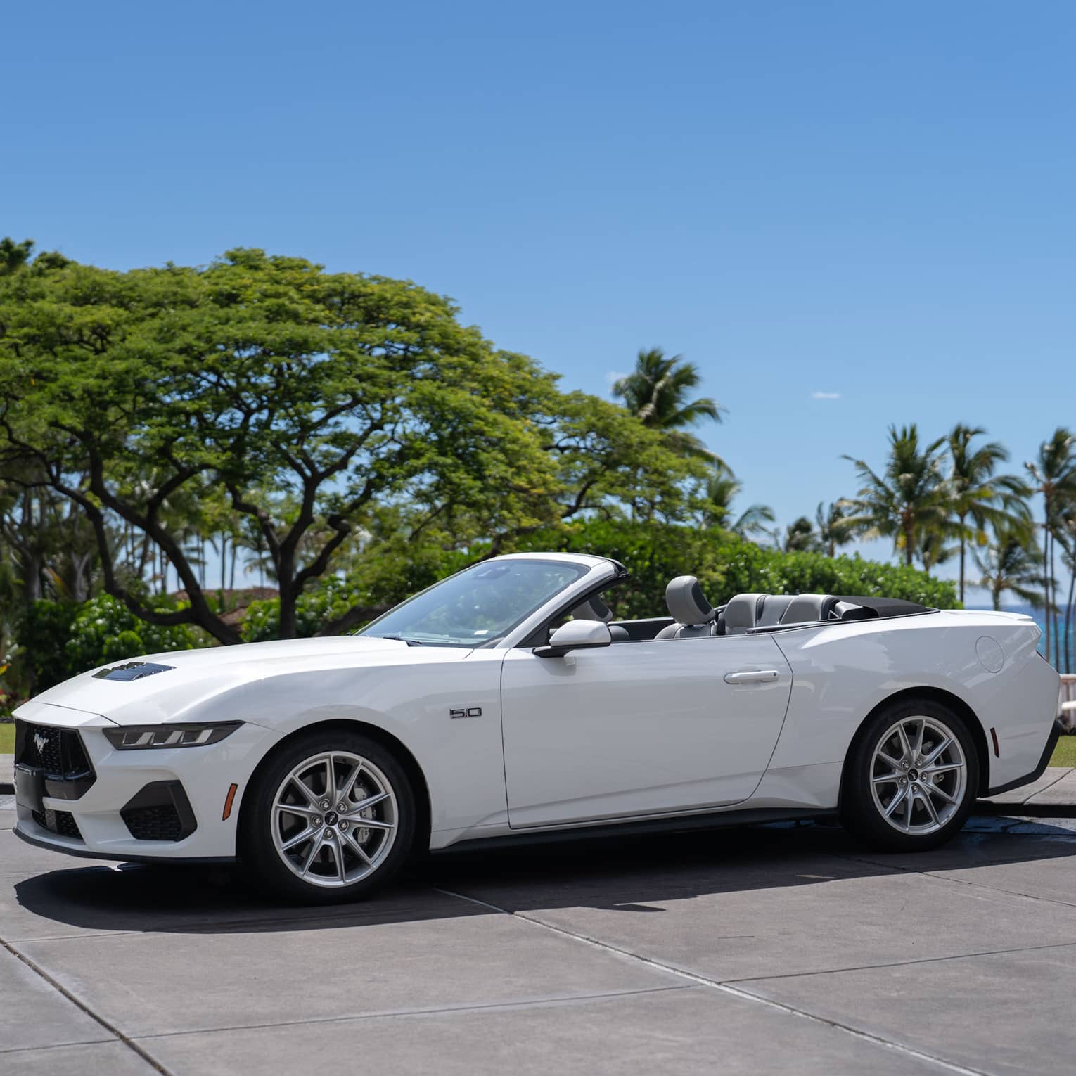 White convertible car parked in front of tropical beach setting