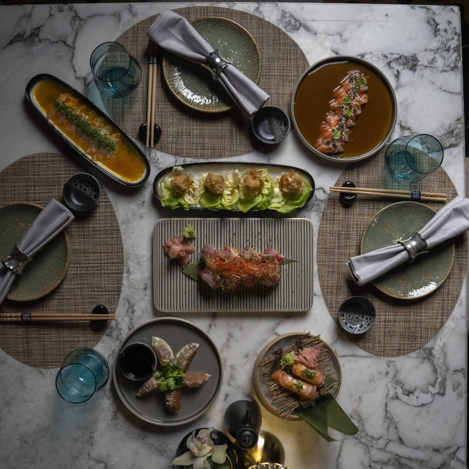 Overhead view of Jappanese Nikkei cuisine on a white marble table set for three