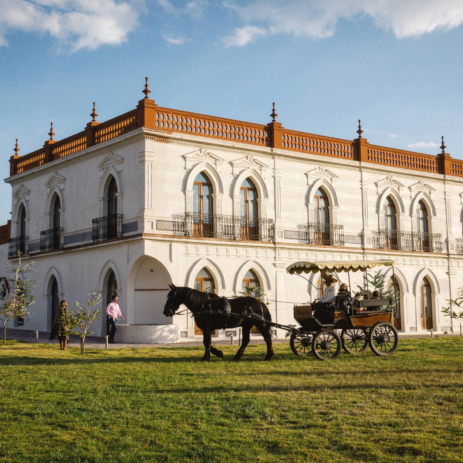 Guests enjoying a horse-drawn carriage ride around a large white building with several beautifully carved arched doorframes.