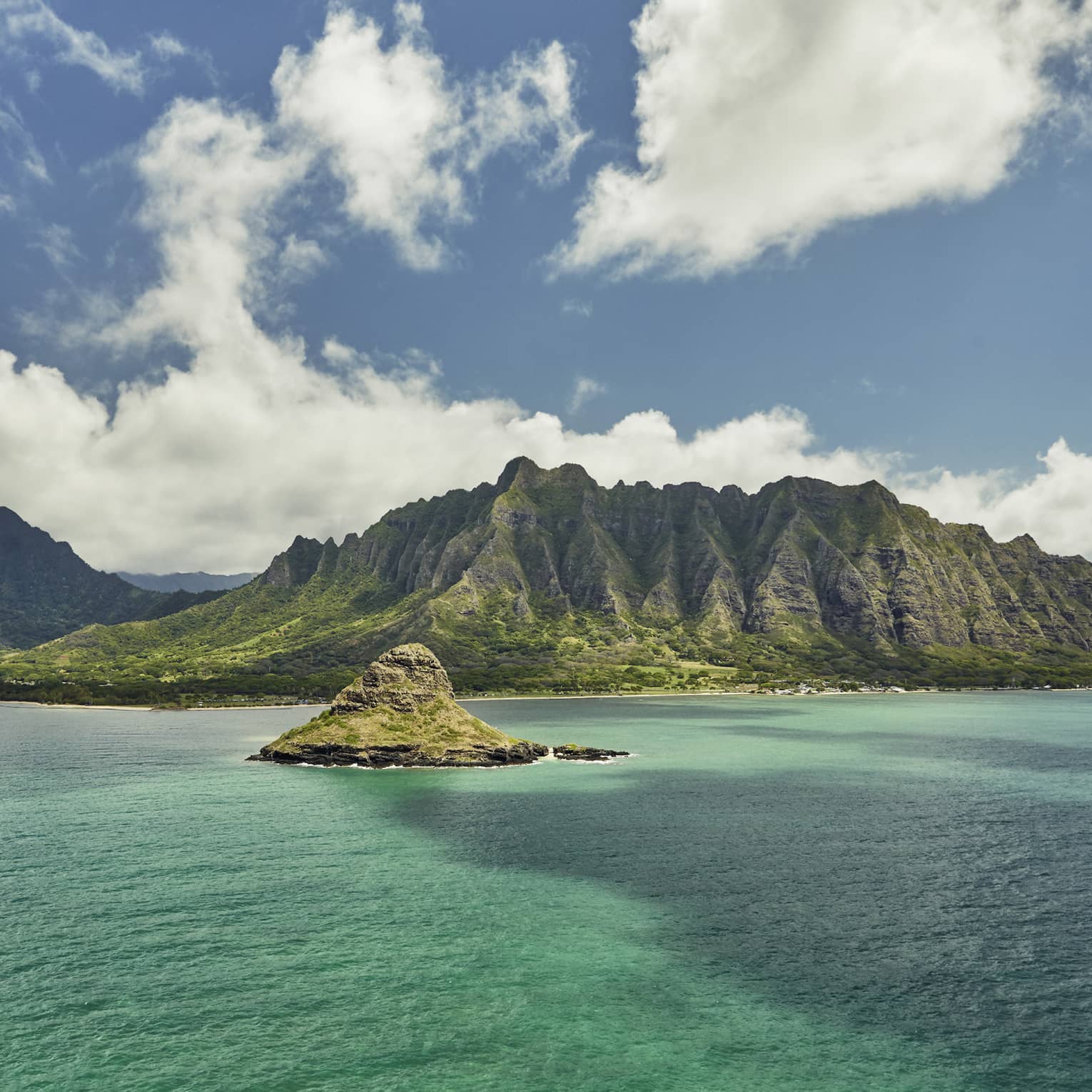 Sweeping green Oahu, Hawaii mountains, small island over turquoise lagoon, white clouds