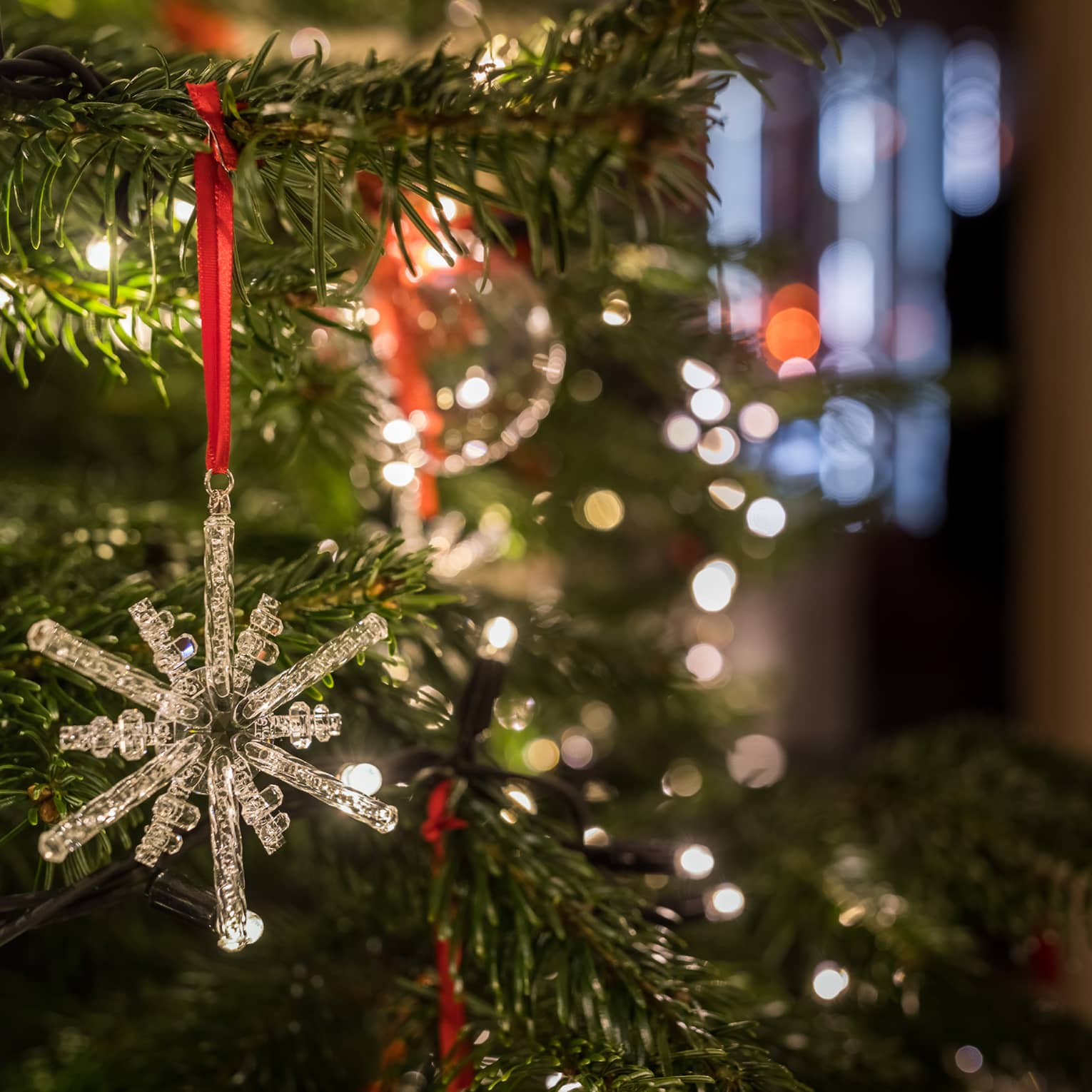Close-up of a crystal snowflake ornament hanging on a Christmas tree with festive lights in the background