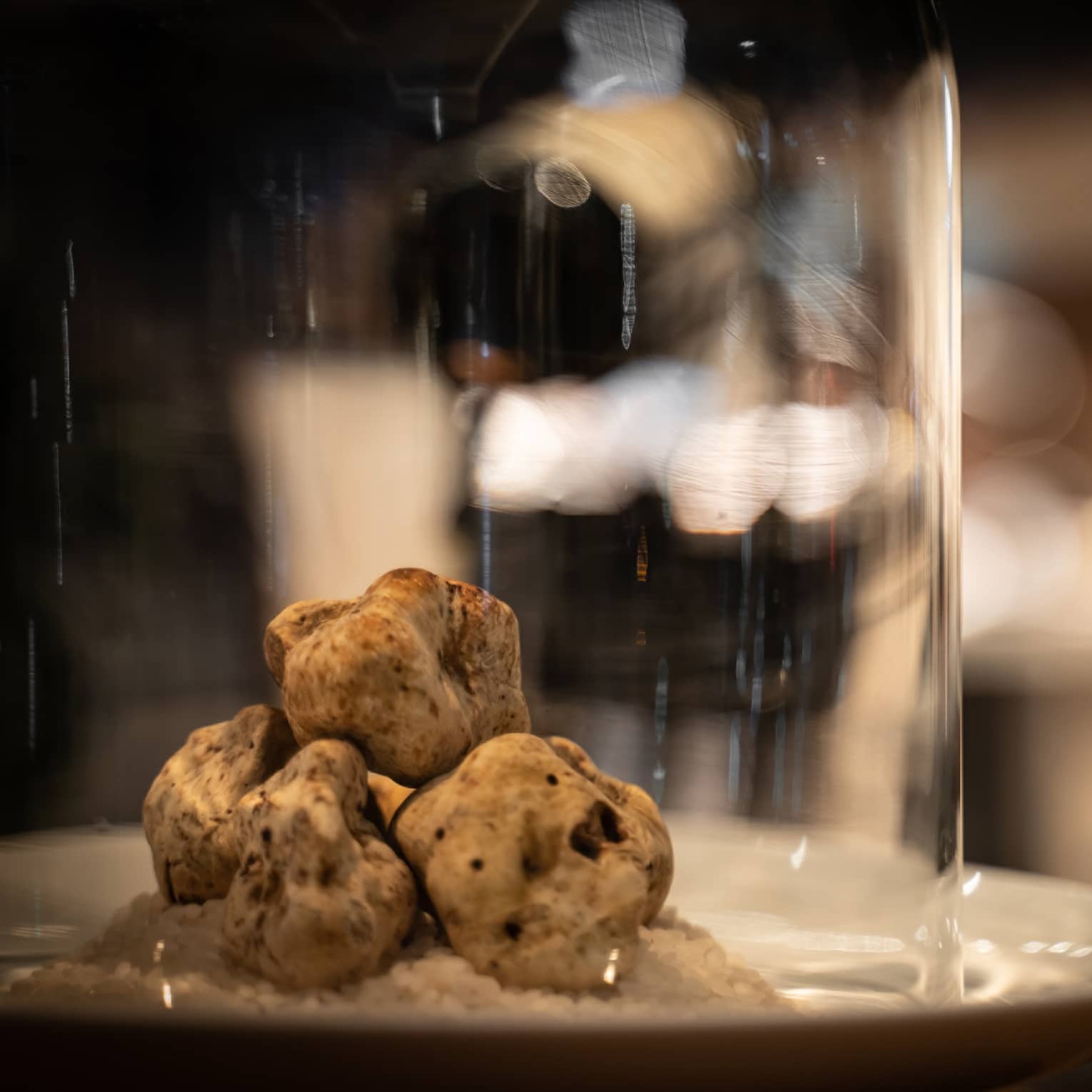 Three irregular truffles stacked on a white plate under a cloche
