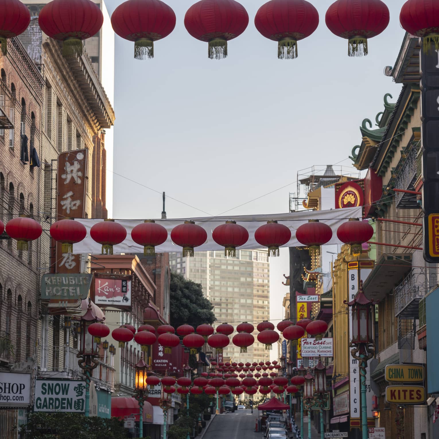 View from the bottom of a Chinatown street lined with restaurants and shops, round red lanterns strung across overhead. 