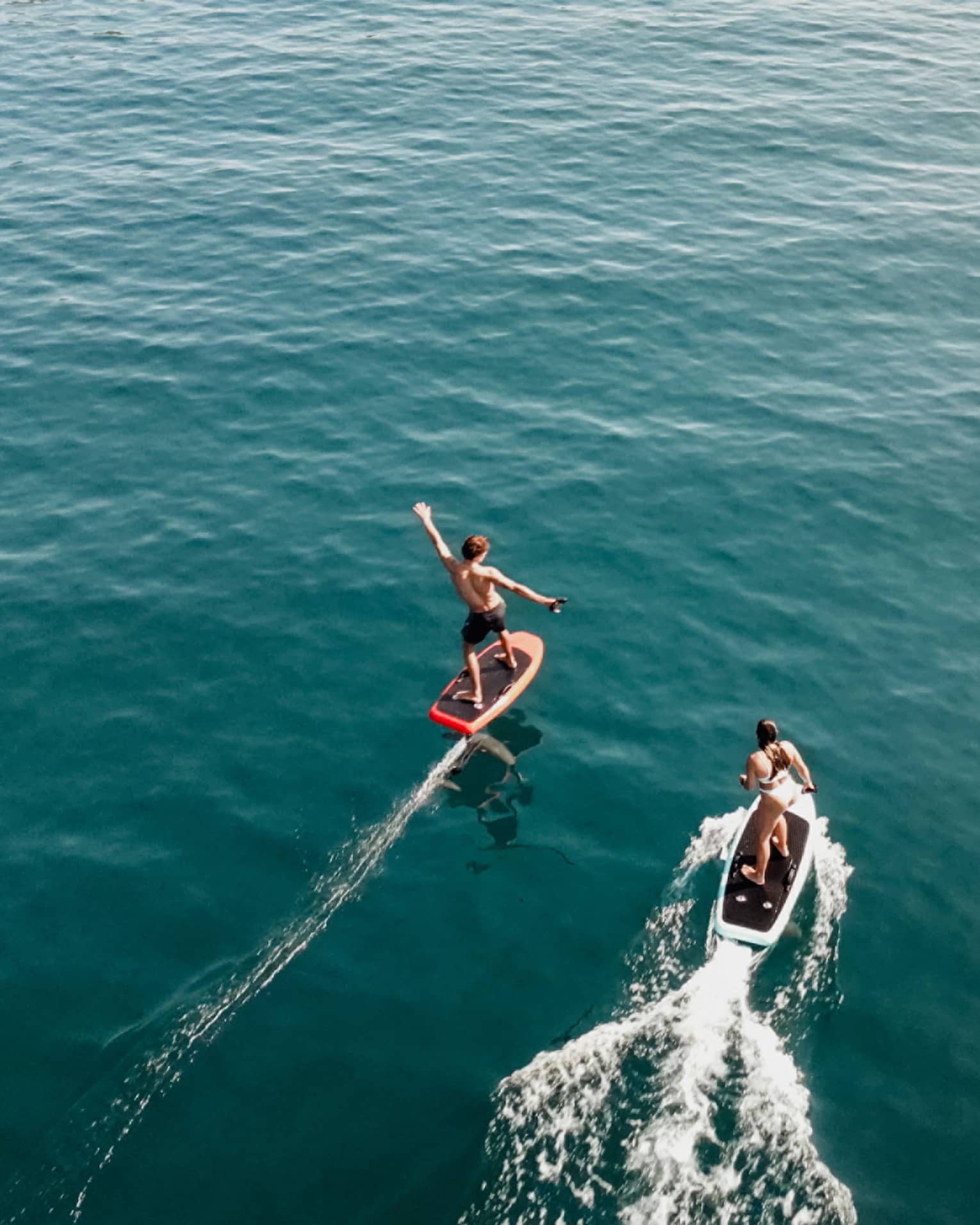 Aerial view of two people riding e0foil surfboards on blue-green water