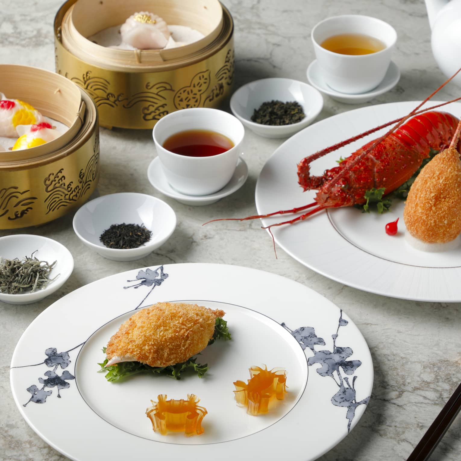 Plain white cups of tea are surrounded by bowls of dried tea leaves, baskets of dumplings and plates of lobster and seafood.
