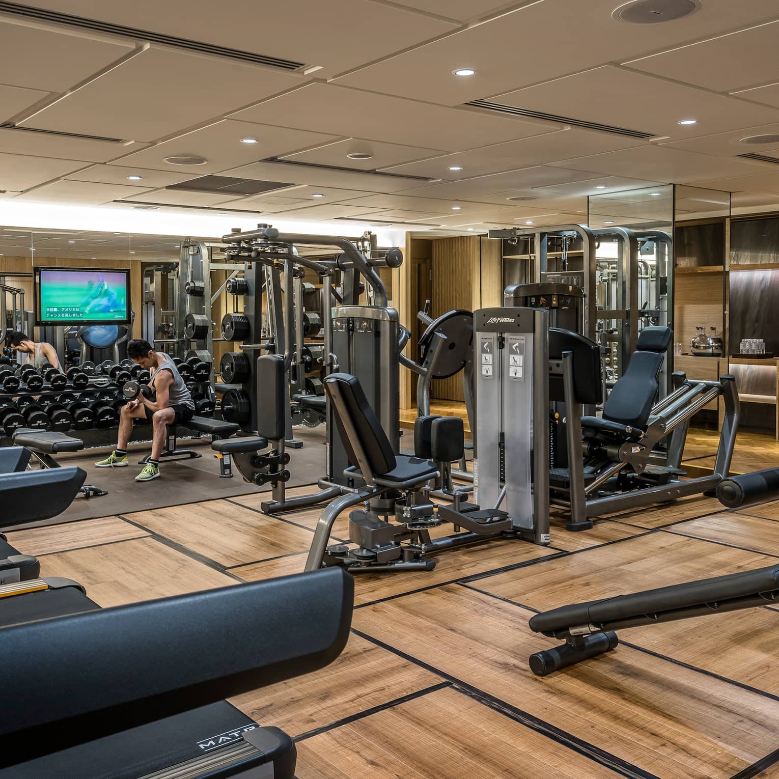 Man sits on bench, lifts weights on Fitness Centre by cardio machines 