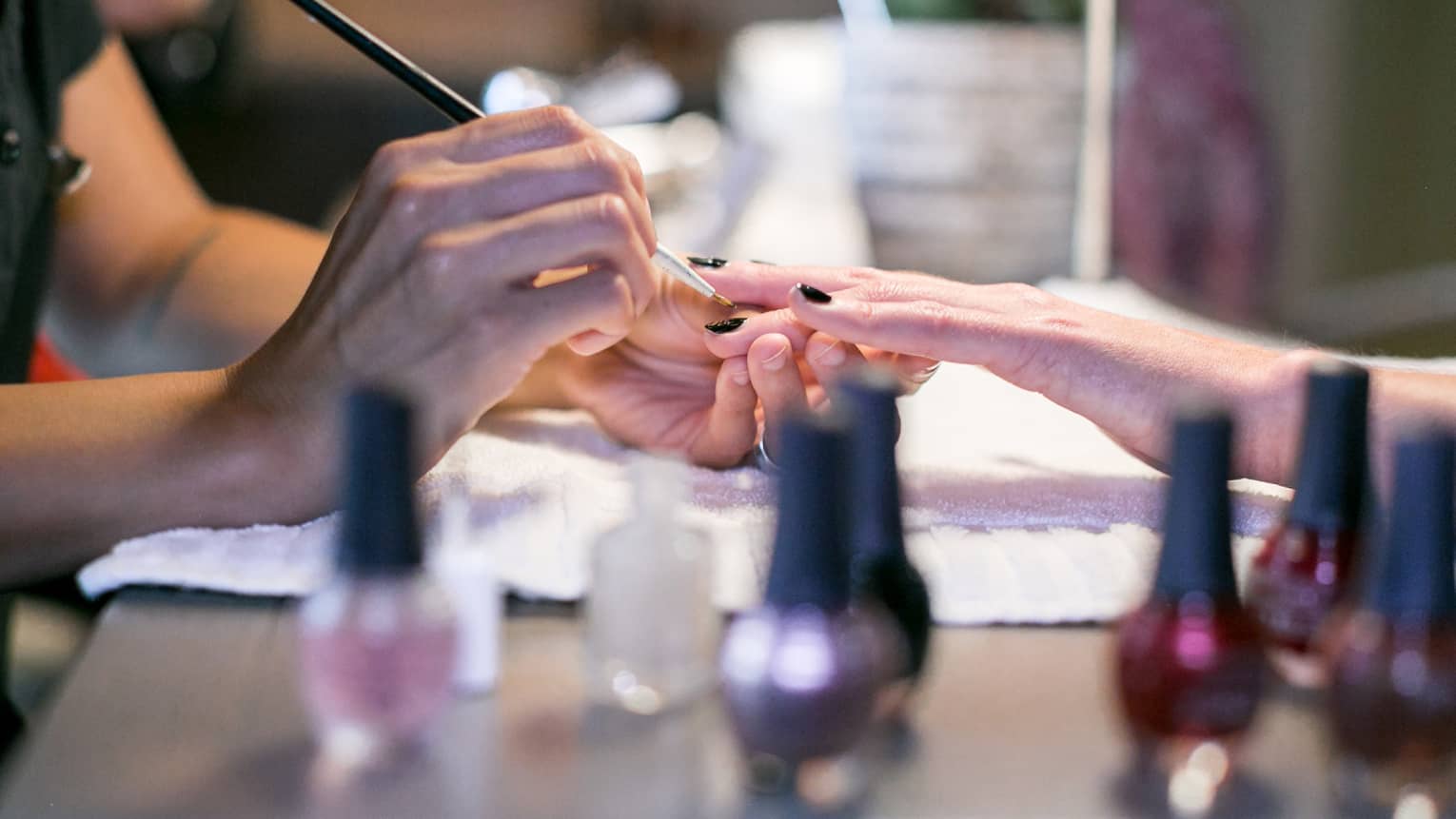 Close-up of spa staff painting woman's nails at manicure table